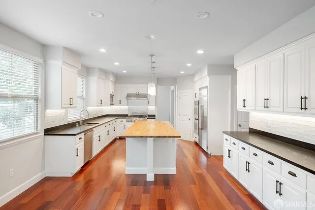 a large kitchen with stainless steel appliances kitchen island granite countertop wooden floors and white cabinets