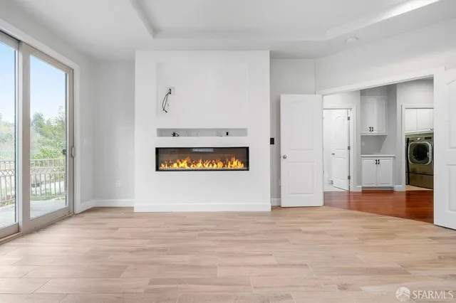a view of an empty room with window and kitchen view