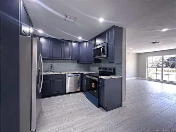 a large kitchen with a stove top oven a sink dishwasher a refrigerator and black cabinets with wooden floor