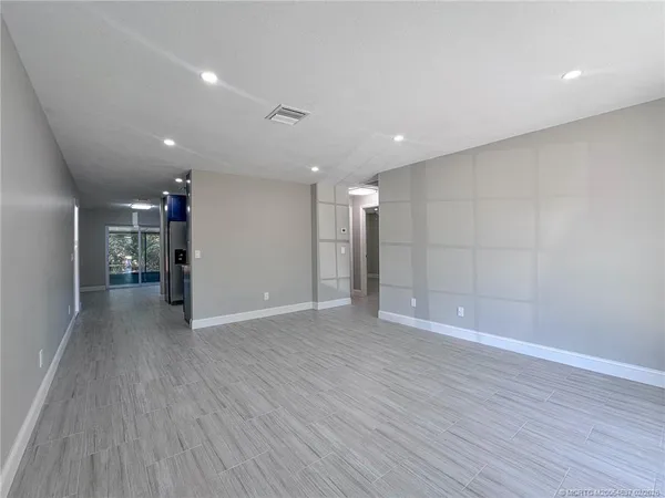 a view of an empty room with wooden floor and a kitchen