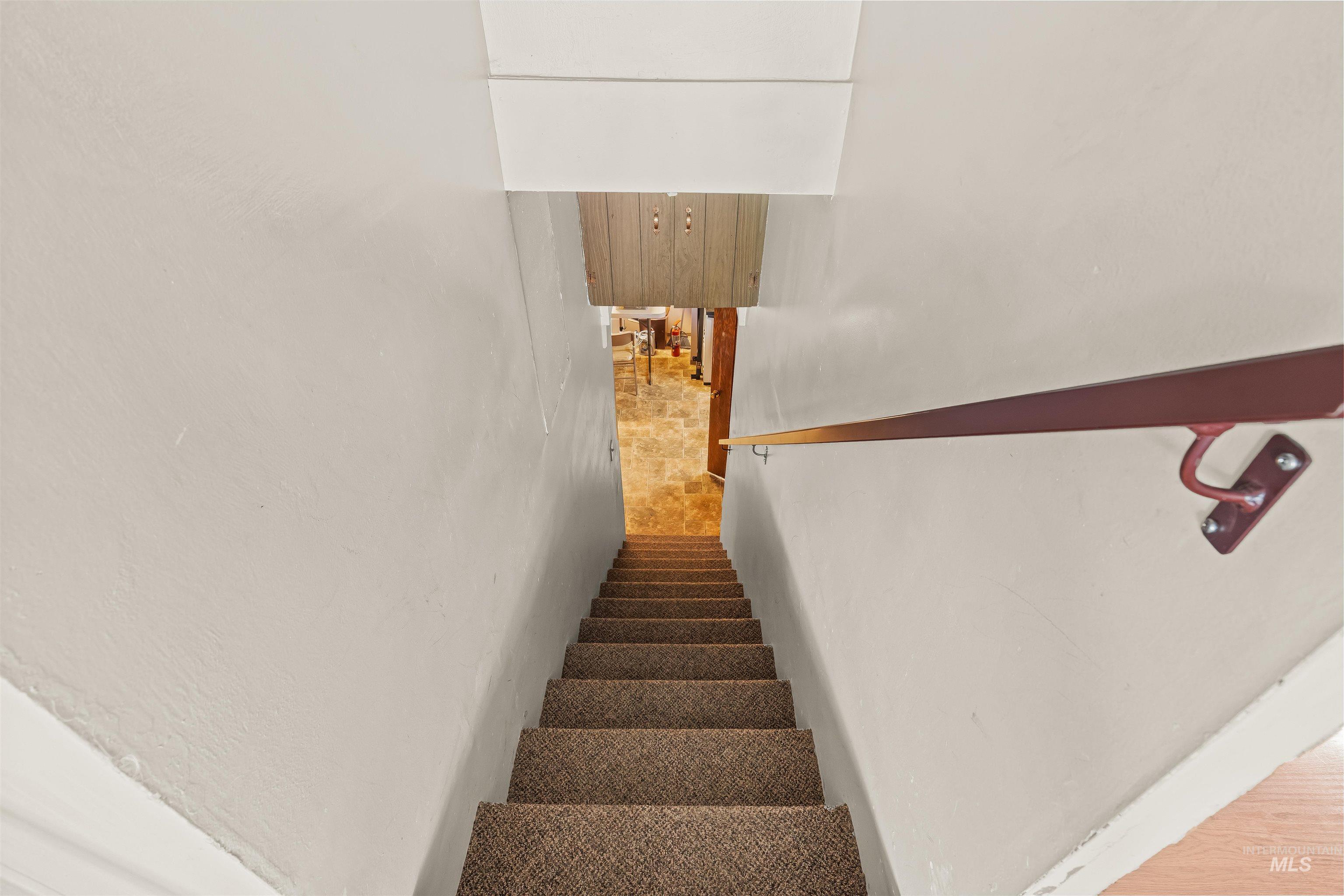 1663 9th Avenue Lewiston, ID 83501 - Photo 25 of 36 Carpeted staircase with a wood handrail descending to a lower level featuring tile flooring and wood-paneled walls