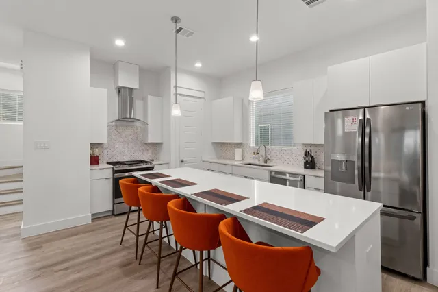 a kitchen with stainless steel appliances granite countertop a refrigerator a sink a stove a dining table and chairs