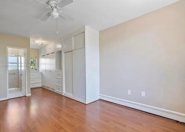 an empty room with wooden floor a ceiling fan and kitchen view