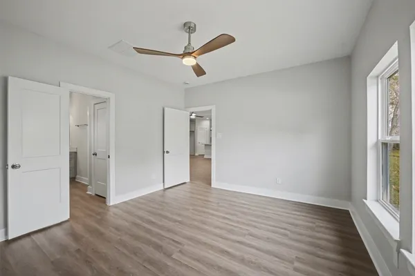 an empty room with wooden floor a ceiling fan and windows