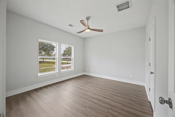 an empty room with wooden floor ceiling fan and windows