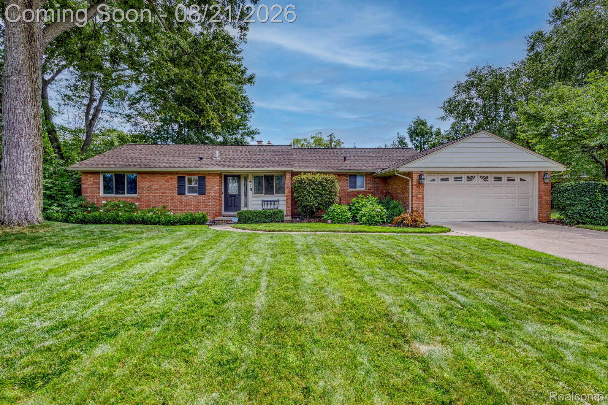 Brick exterior with an attached garage, paved driveway, and mature landscaping