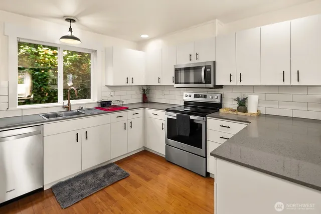 a kitchen with stainless steel appliances granite countertop a sink dishwasher stove and white cabinets with wooden floor
