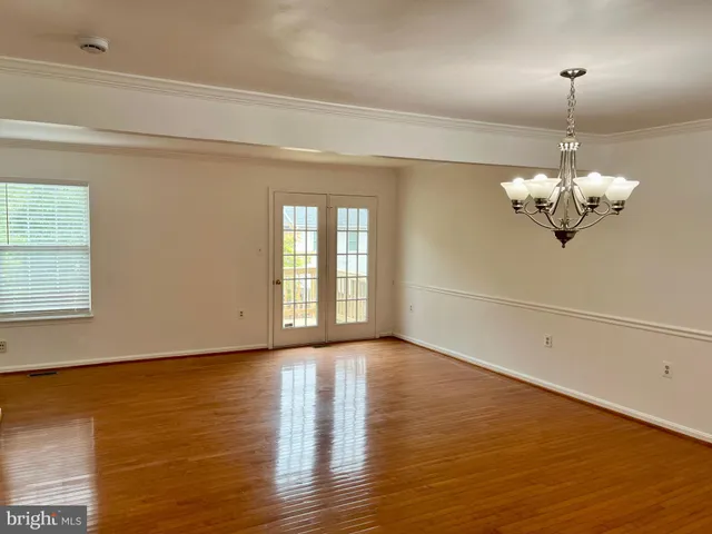 an empty room with wooden floor chandelier fan and windows