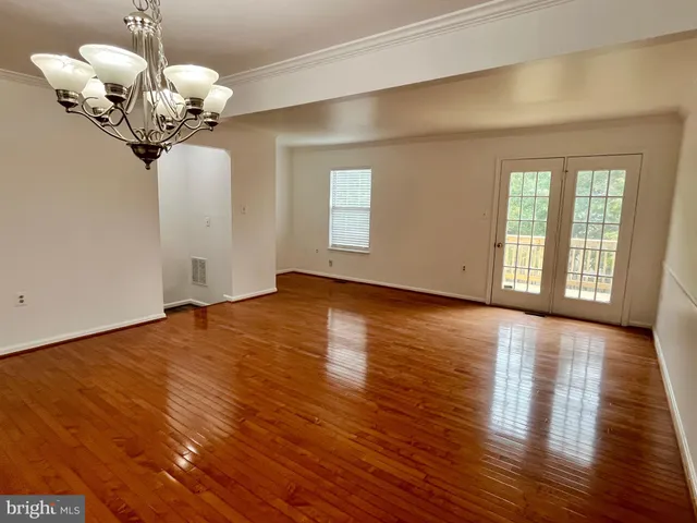 a view of an empty room with wooden floor and chandelier