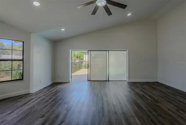 an empty room with wooden floor chandelier fan and windows