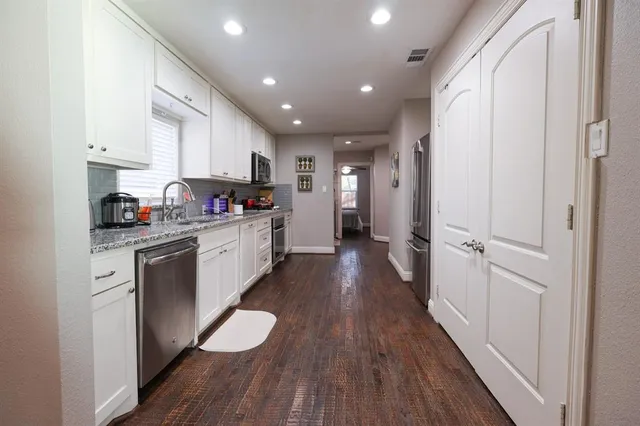 a kitchen with a hard wood floor white cabinets and stainless steel appliances
