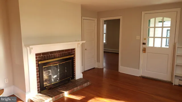 a view of an empty room with wooden floor fireplace and a window