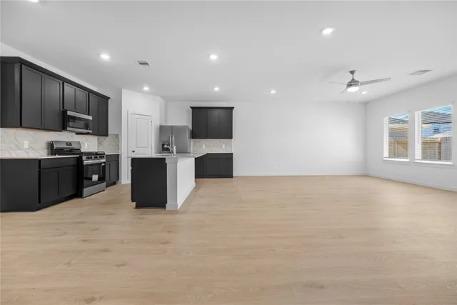 a large kitchen with stainless steel appliances a large counter top a stove a refrigerator a sink a microwave and cabinets