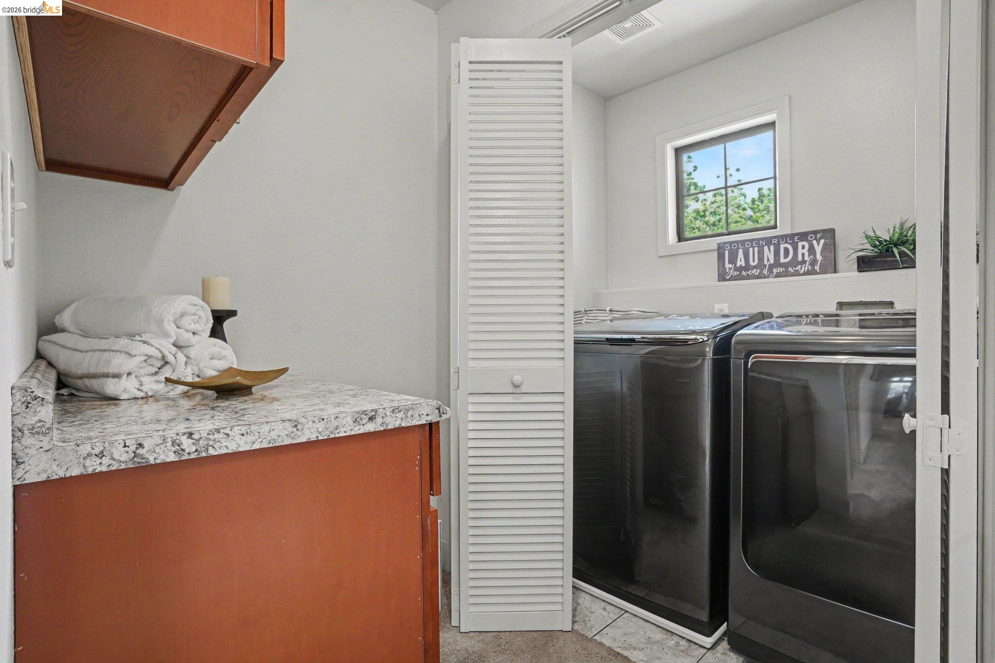 1433 Myrtle Street Oakland, CA 94607 - Photo 19 of 25 Laundry area featuring a window, built-in shelving, wood-finish cabinetry, and a speckled countertop