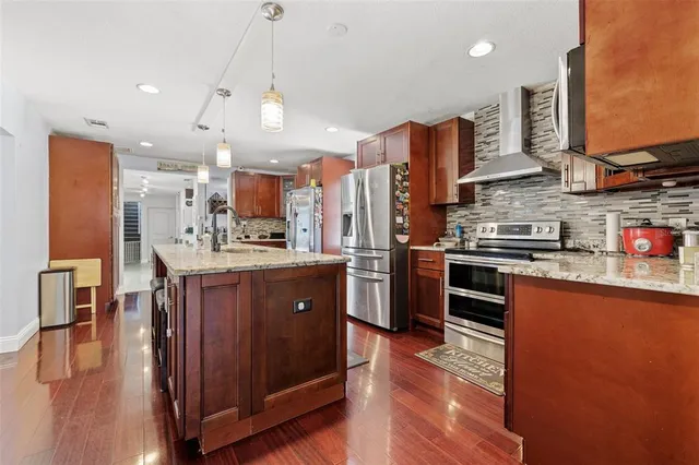 a kitchen with stainless steel appliances granite countertop a refrigerator a sink dishwasher a oven and a dining table with wooden floor