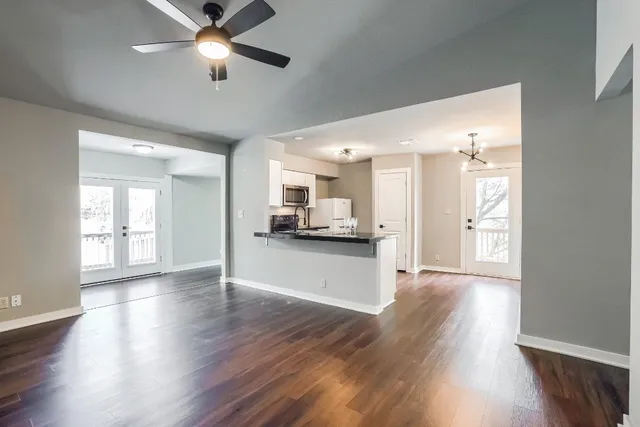 a view of an empty room and kitchen with wooden floor and a window