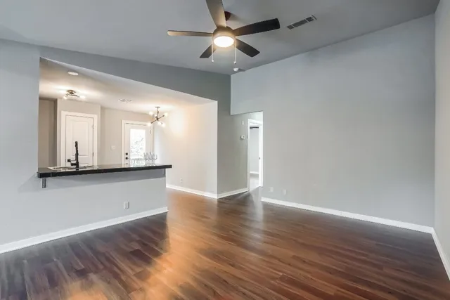 a view of an empty room and kitchen with wooden floor