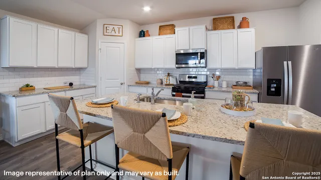 a kitchen with stainless steel appliances granite countertop a sink a stove a microwave a refrigerator and white cabinets with wooden floors