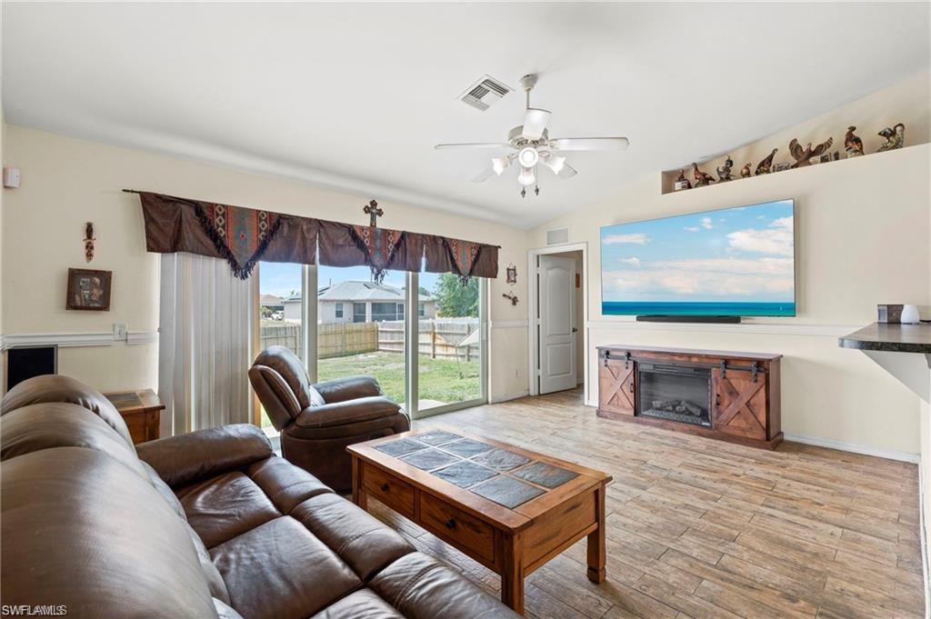 3303 32nd Street Southwest Lehigh Acres, FL 33976 - Photo 3 of 35 a living room with furniture a flat screen tv and floor to ceiling window
