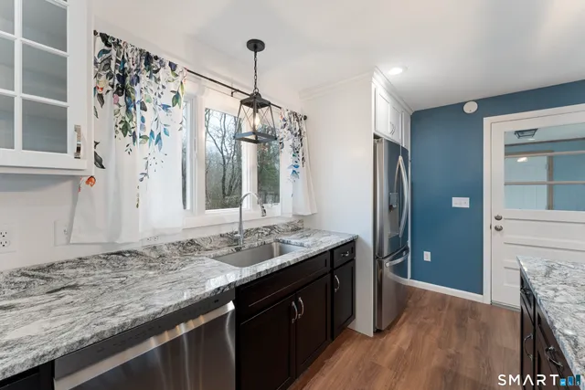 a kitchen with stainless steel appliances granite countertop a sink a refrigerator and a wooden floor