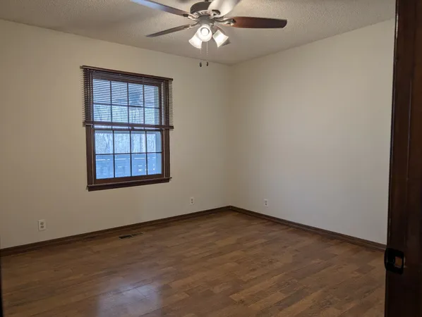 an empty room with wooden floor chandelier fan and windows