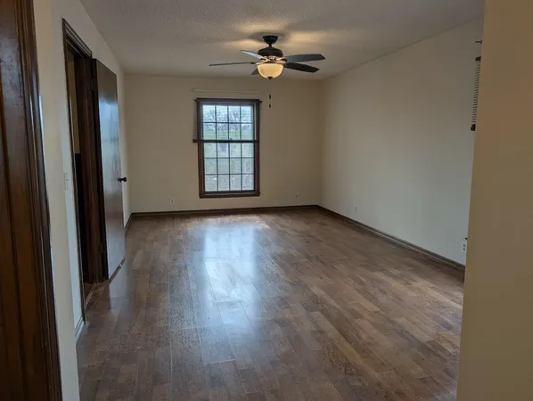 an empty room with wooden floor chandelier fan and windows