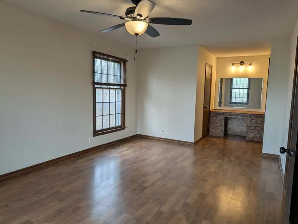 an empty room with wooden floor fan and windows