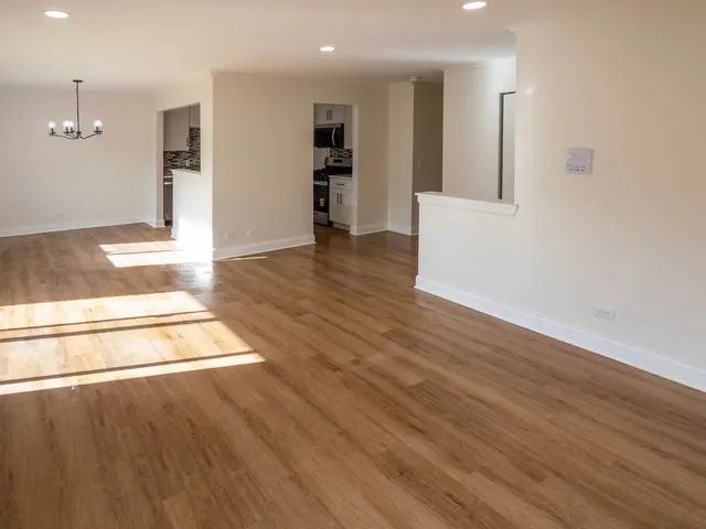 an empty room with wooden floor and kitchen view
