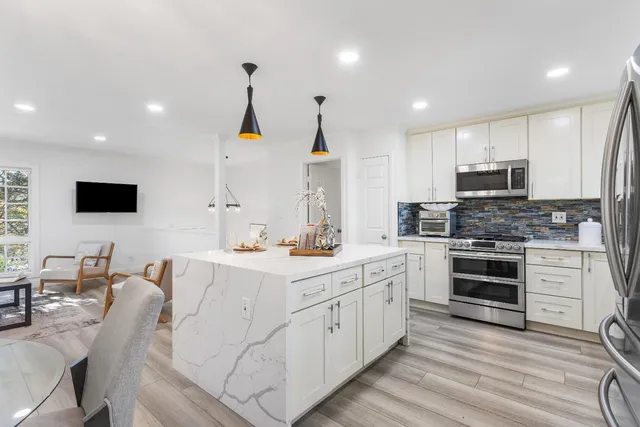 a kitchen with stainless steel appliances a stove top oven a sink dishwasher a refrigerator and a dining table with wooden floor