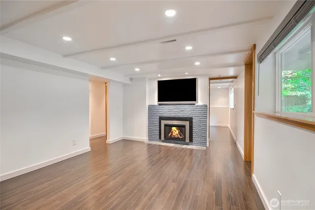 a view of an empty room with wooden floor a fireplace and a window