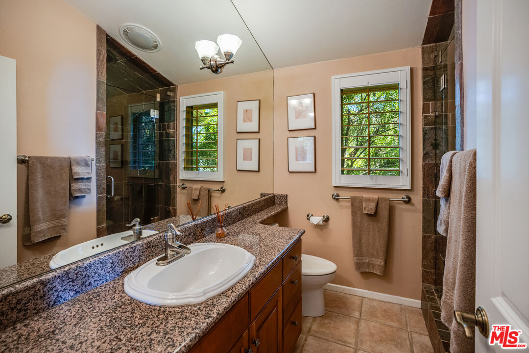 1643 La Vista Del Oceano Santa Barbara, CA 93109 - Photo 27 of 36 a bathroom with a granite countertop sink a large mirror a toilet and a shower