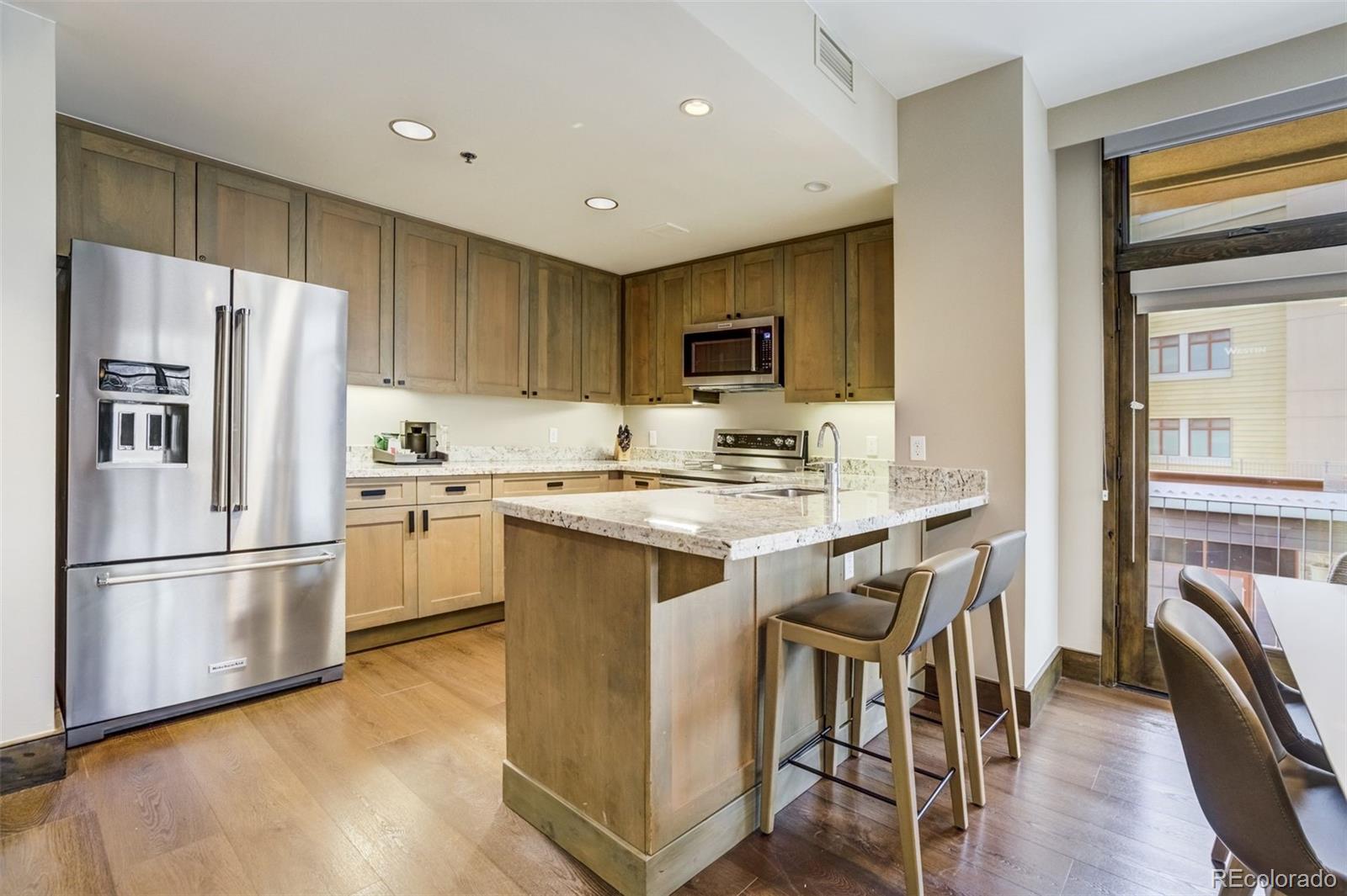 126 Riverfront Lane, Unit 200 Avon, CO 81620 - Photo 9 of 49 a kitchen with a refrigerator a stove top oven a sink dishwasher and white cabinets with wooden floor