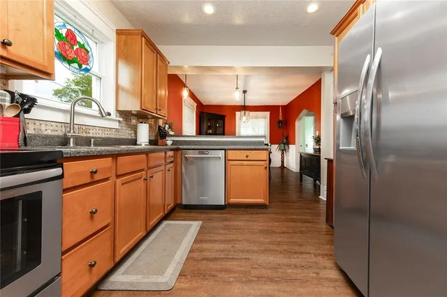 a kitchen with stainless steel appliances granite countertop a refrigerator a sink dishwasher and white cabinets with wooden floor