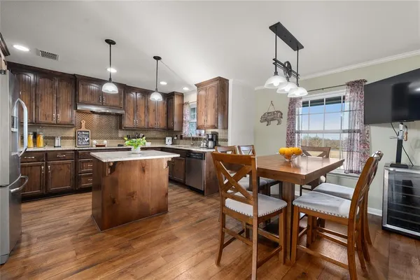 a kitchen with stainless steel appliances kitchen island granite countertop a table chairs and a wooden floor