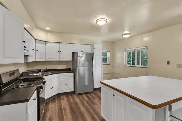 a kitchen with granite countertop a refrigerator a stove a sink dishwasher and white countertops with wooden floor