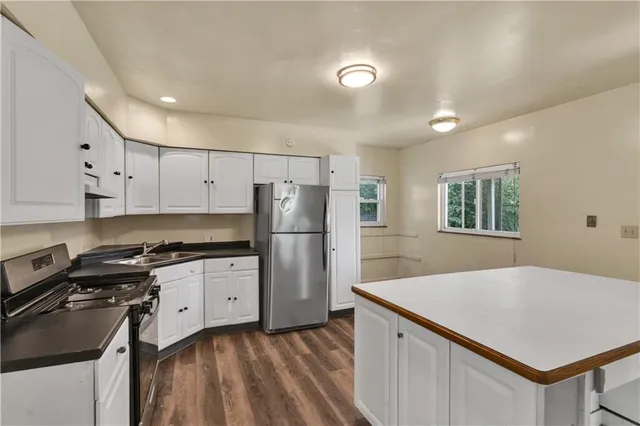 a kitchen with granite countertop a refrigerator a stove a sink dishwasher and white countertops with wooden floor