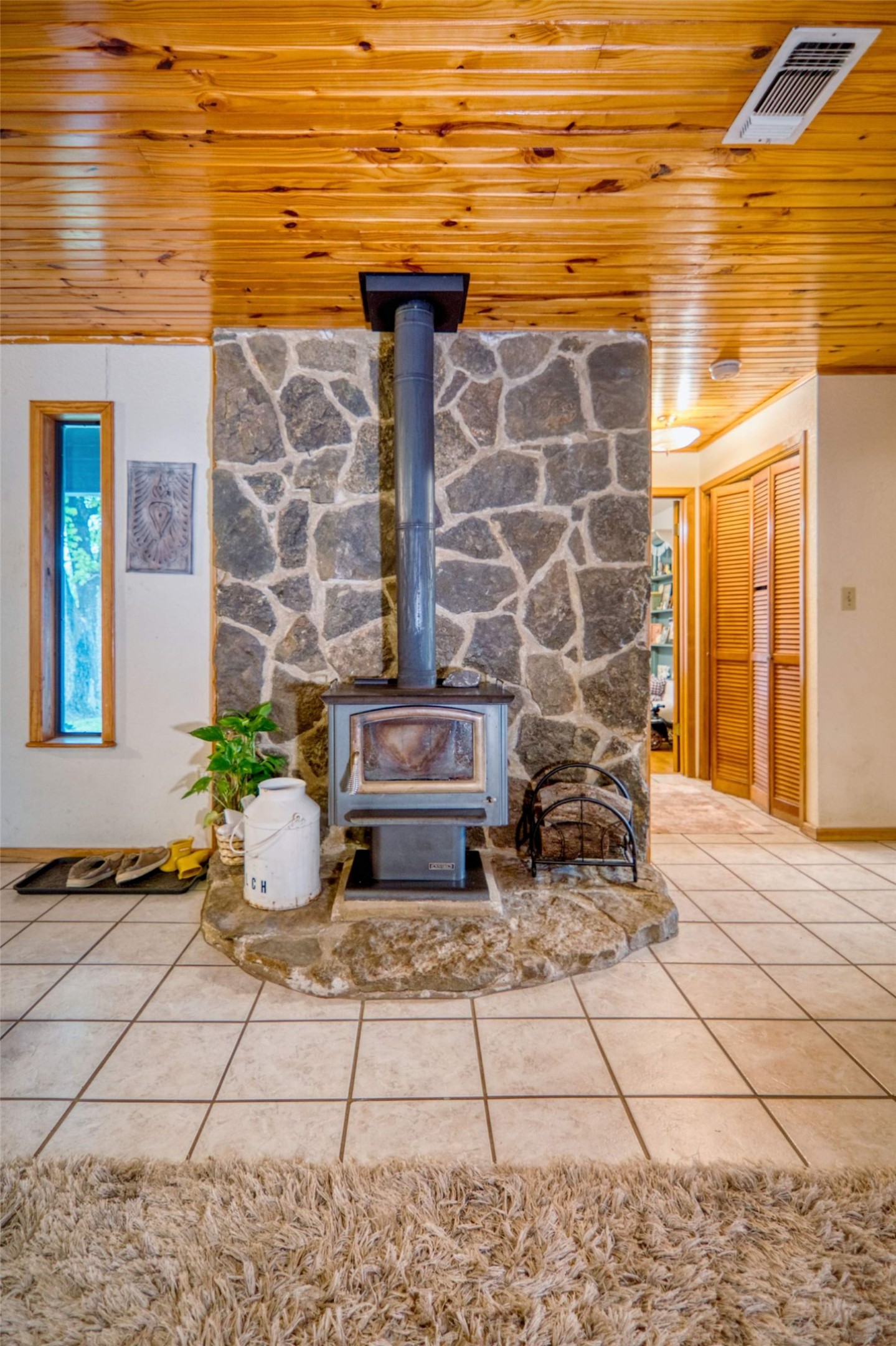 904 Bluebonnet Road Mason, TX 76856 - Photo 12 of 28 Stone-clad wood-burning stove with a raised hearth, featuring a wood-paneled ceiling, tile flooring, and louvered bi-fold doors