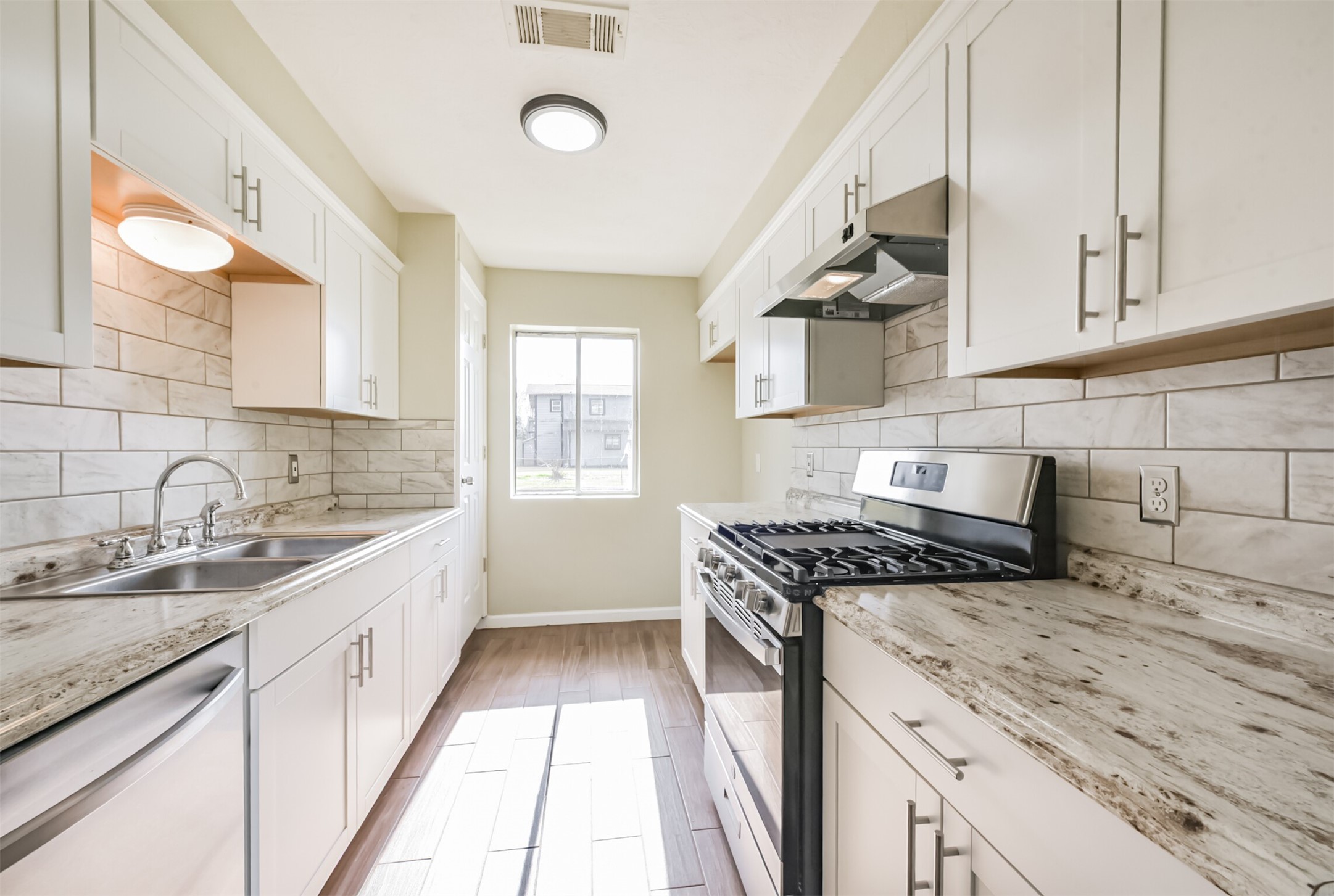 2390 Sarah Street Beaumont, TX 77705 - Photo 11 of 42 Bright, modern kitchen with light cabinetry, stainless steel appliances, and marbled countertops. Features a window for natural light and wood-style flooring.