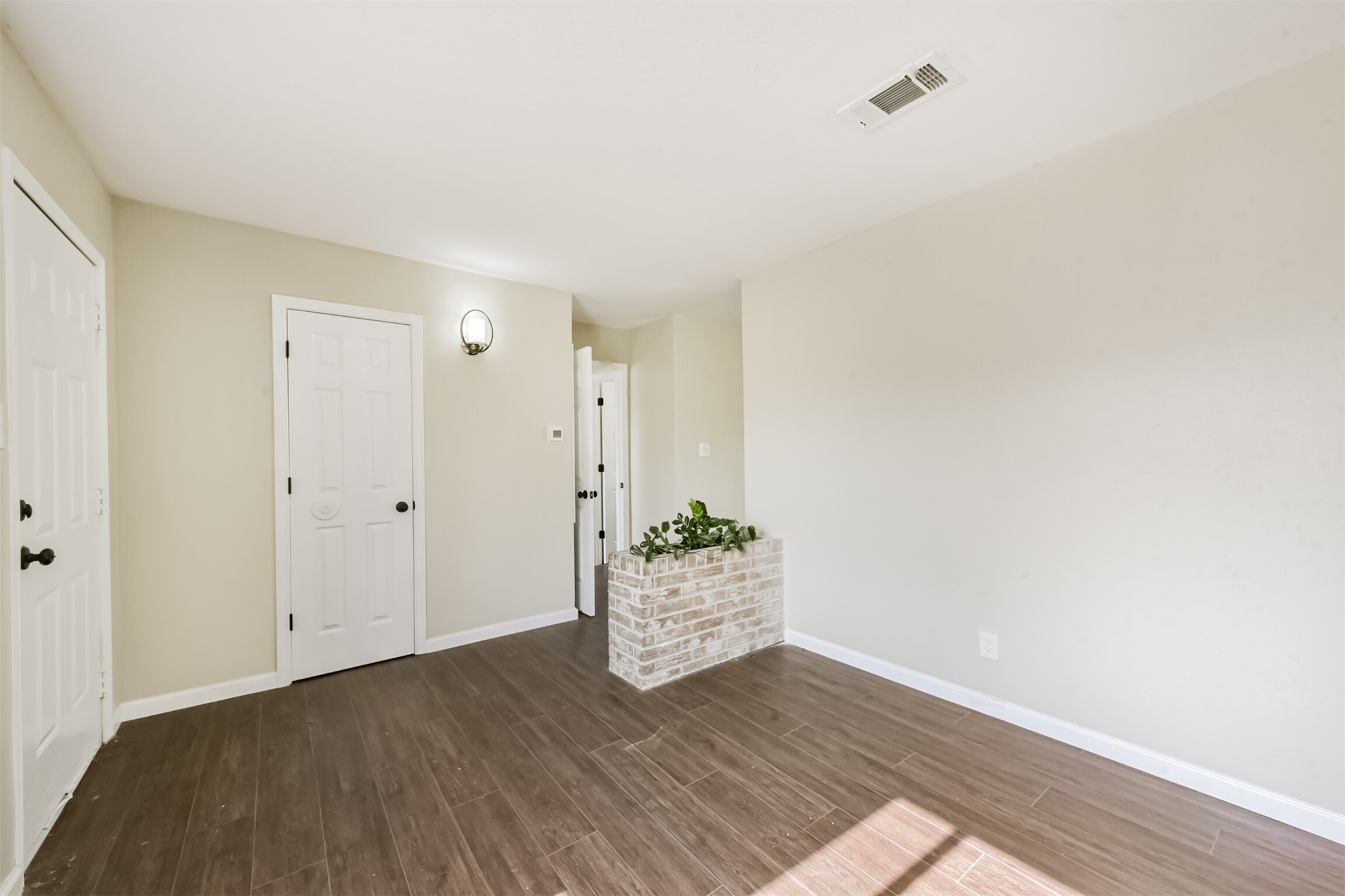2390 Sarah Street Beaumont, TX 77705 - Photo 6 of 42 This room features light-colored walls, dark wood flooring, and a small brick planter. It has two white doors, a wall-mounted light fixture, and ample natural light, creating a bright and inviting space.