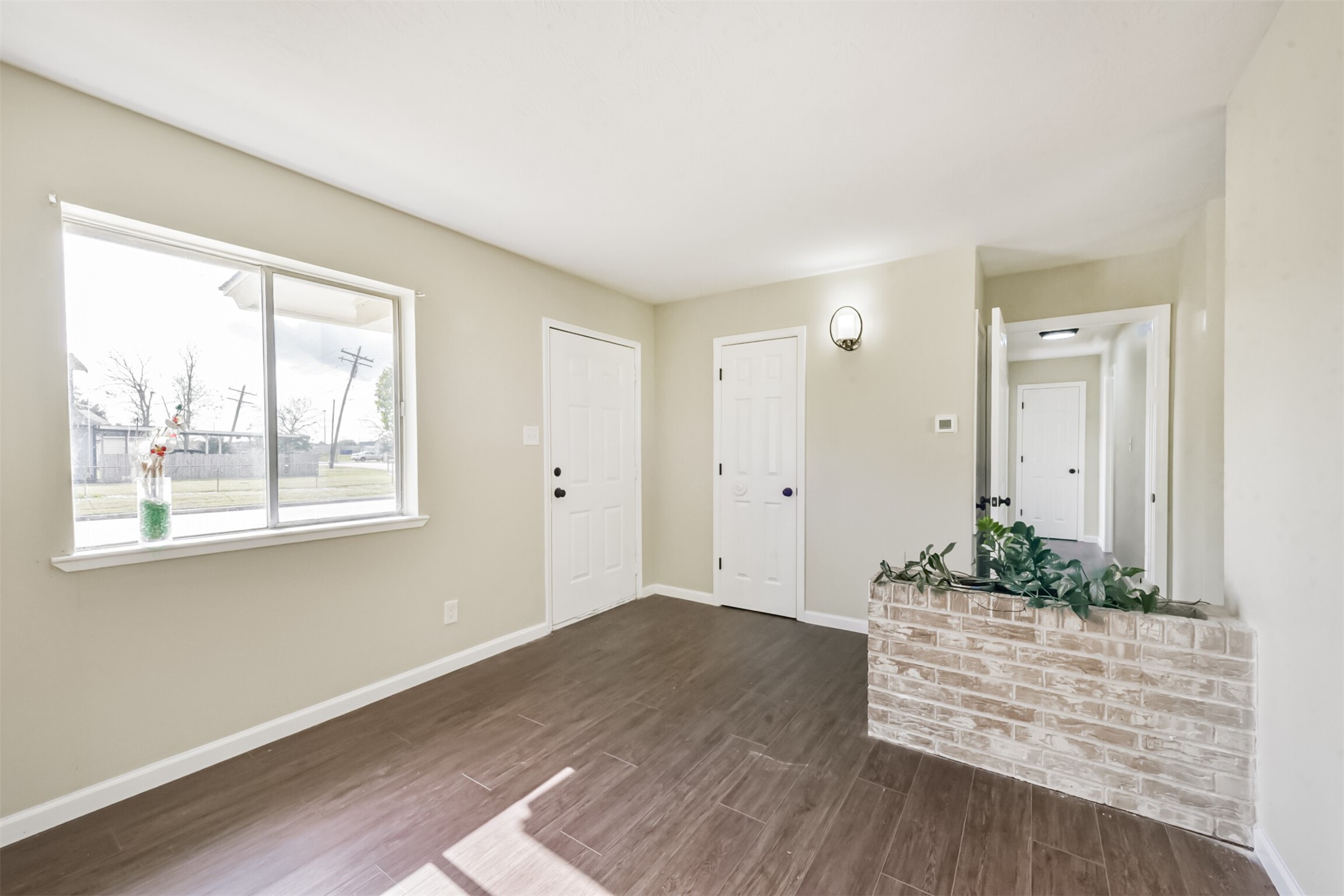 2390 Sarah Street Beaumont, TX 77705 - Photo 7 of 42 Bright room with large window, light walls, and wood flooring. Features a brick planter and leads to a hallway with multiple doors. Ideal for a cozy, welcoming entrance or living space.