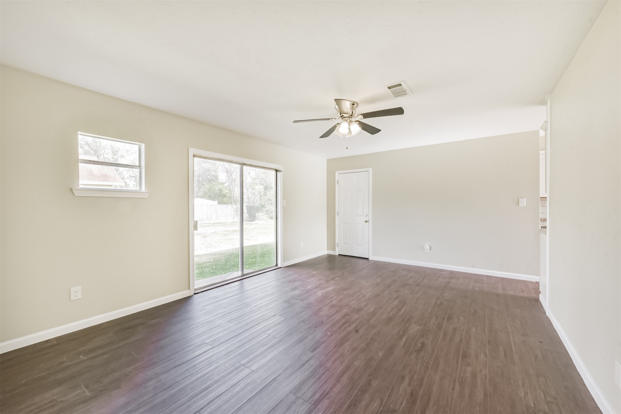2390 Sarah Street Beaumont, TX 77705 - Photo 8 of 42 This room is bright and spacious with neutral walls and dark wood flooring. It features a ceiling fan, sliding glass doors leading to a backyard, and a small window for additional natural light.