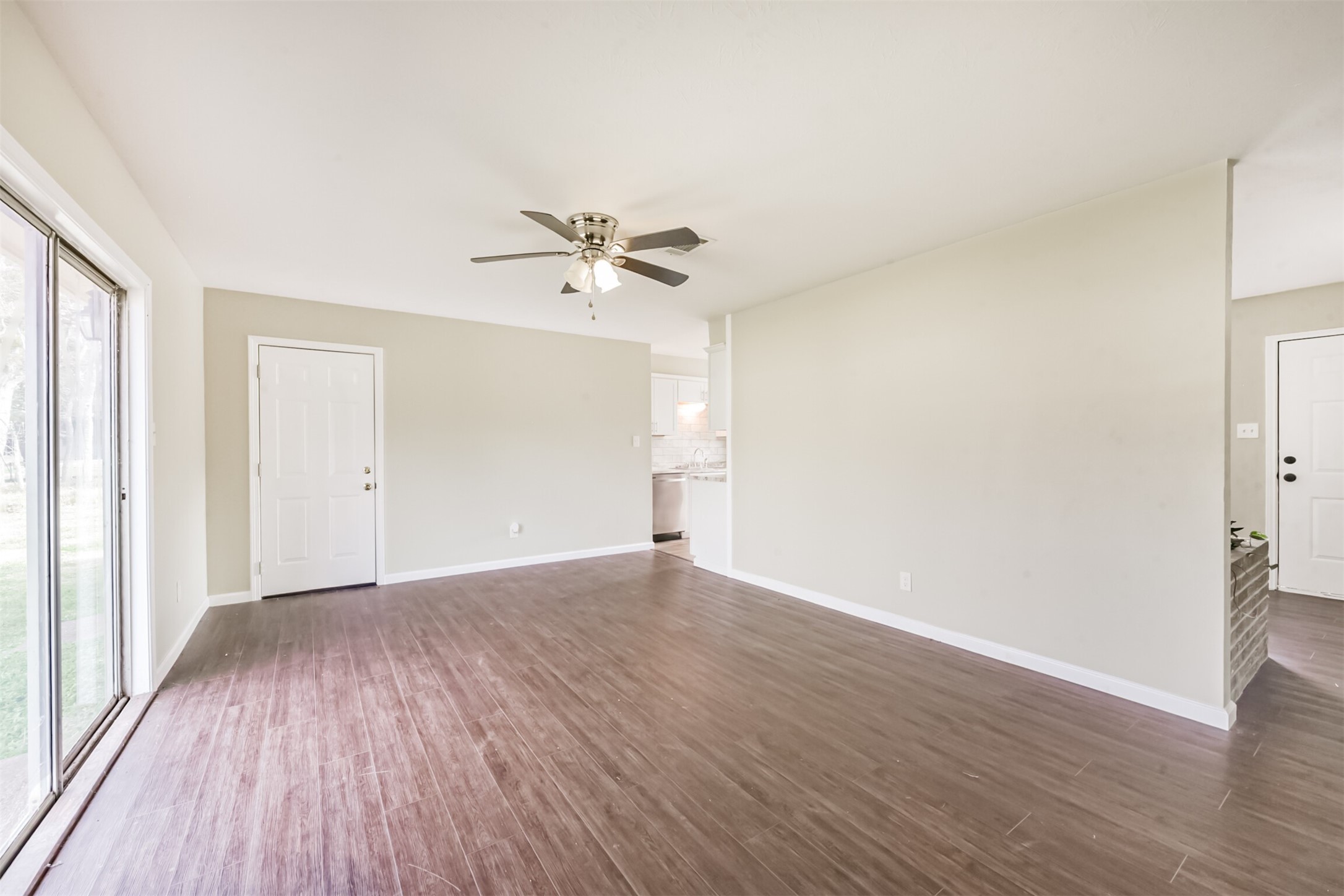 2390 Sarah Street Beaumont, TX 77705 - Photo 9 of 42 This photo showcases a bright, open living space with wood flooring and neutral walls. It features a ceiling fan, large sliding glass doors leading to the outside, and easy access to the kitchen.