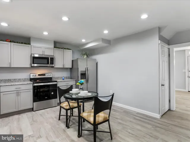 a kitchen with stainless steel appliances granite countertop a stove a sink a microwave a refrigerator with white cabinets and wooden floor