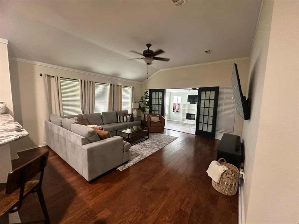 Spacious Living room a ceiling fan, crown molding, dark wood-style floors, vaulted ceiling, and French doors for privacy if needed.