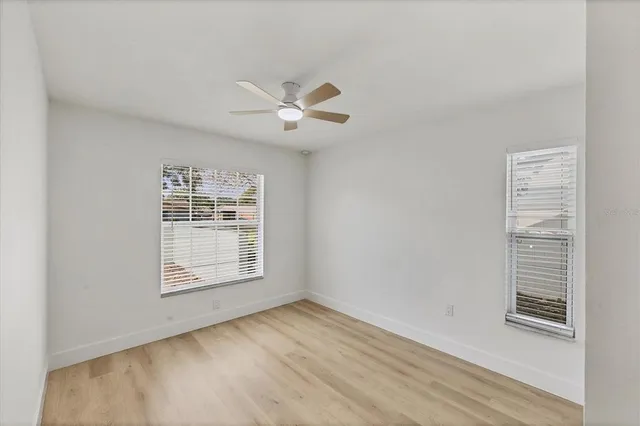 an empty room with wooden floor ceiling fan and windows