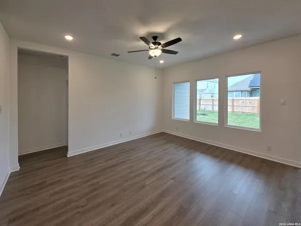 a view of an empty room with wooden floor and a kitchen