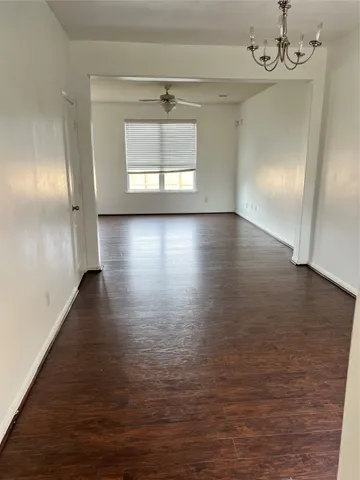 an empty room with wooden floor chandelier and windows
