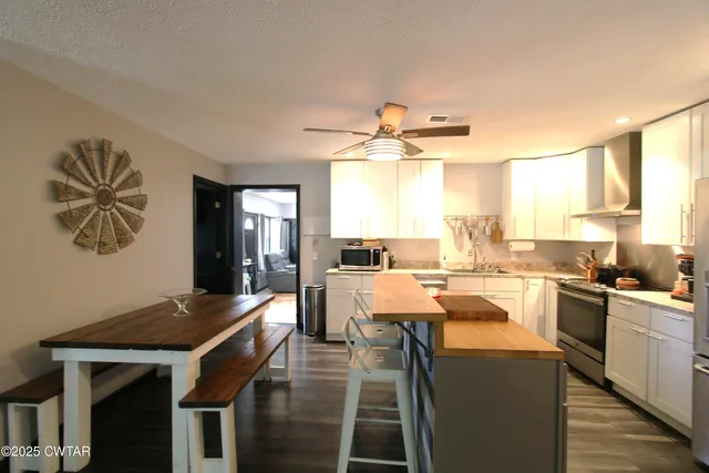 a kitchen with kitchen island a stove a sink a dining table and chairs with wooden floor