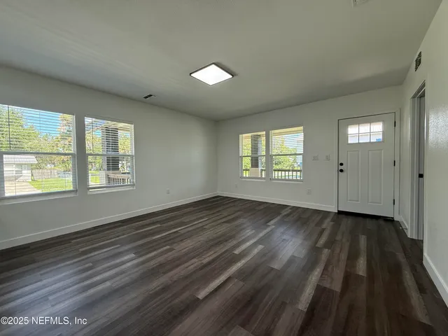 a view of an empty room with wooden floor and a window