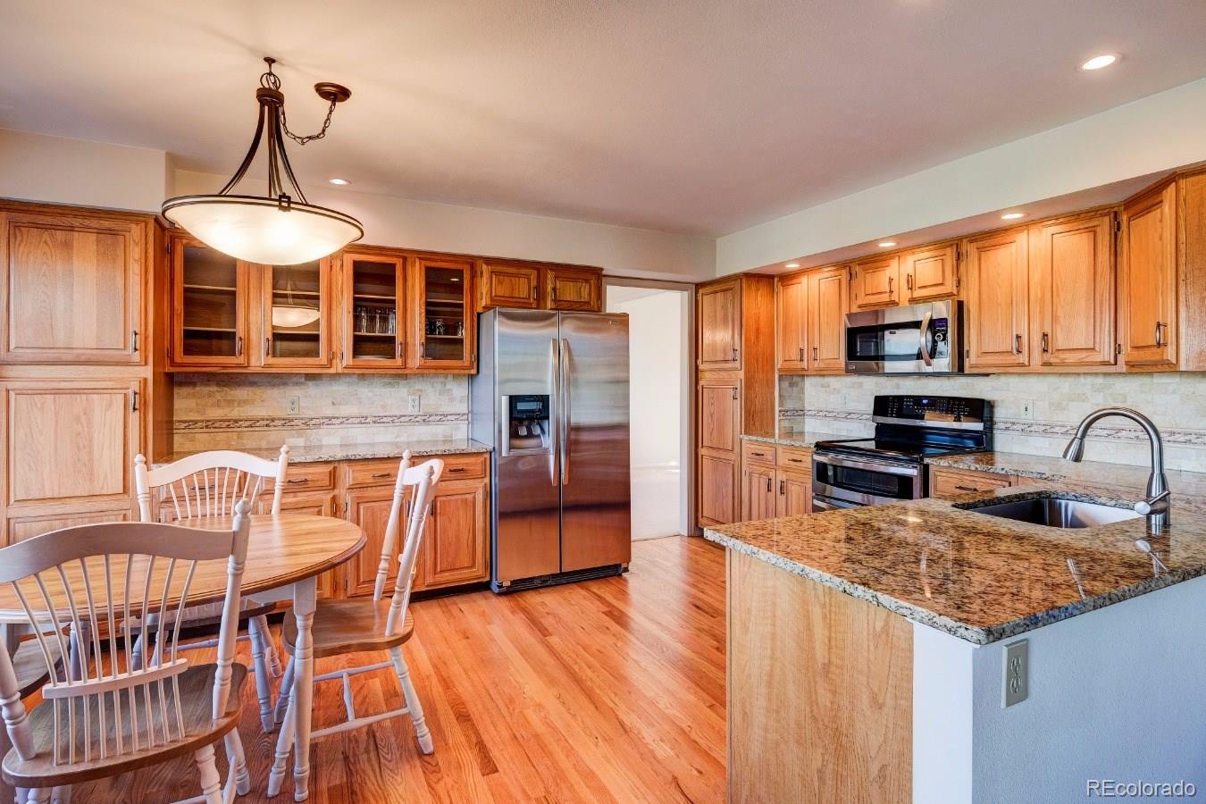 8927 Mountain Laurel Way Highlands Ranch, CO 80126 - Photo 10 of 35 a kitchen with stainless steel appliances granite countertop a kitchen island hardwood floor sink stove dining table and chairs